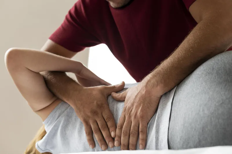 Hände eines Therapeuten bei einer osteopathischen Behandlung am unteren Rücken