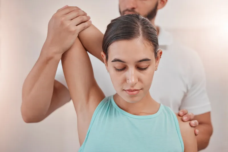 Physiotherapeut führt den Arm einer Patientin in eine Dehnung